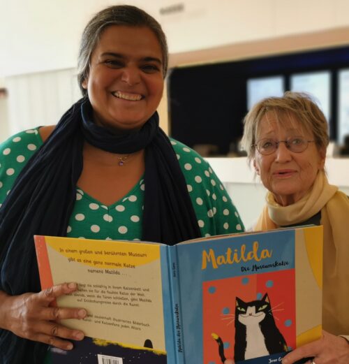 Museumspädagogin und Vorleserin lächeln in die Kamera. Im Vordergrund ist der Buchrücken von Matilda zu sehen.