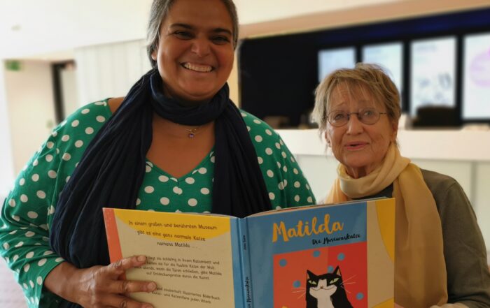 Museumspädagogin und Vorleserin lächeln in die Kamera. Im Vordergrund ist der Buchrücken von Matilda zu sehen.