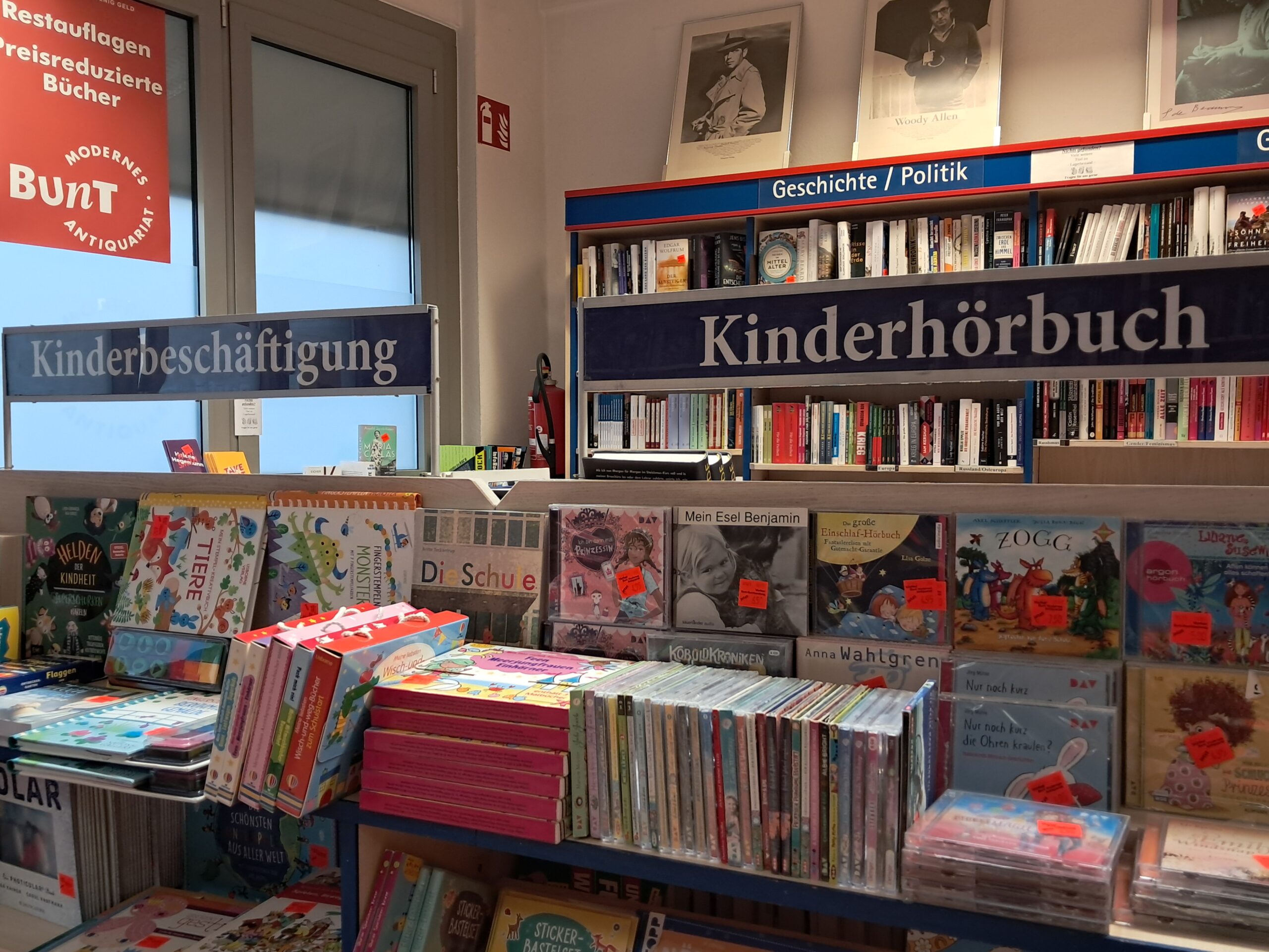 In Regalen sind viele Bücher und Hörbücher gestapelt. Darüber hängt ein Schild mit der Aufschrift "Kinderhörbücher".